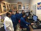 Students in lab coats watching a lab display on a computer